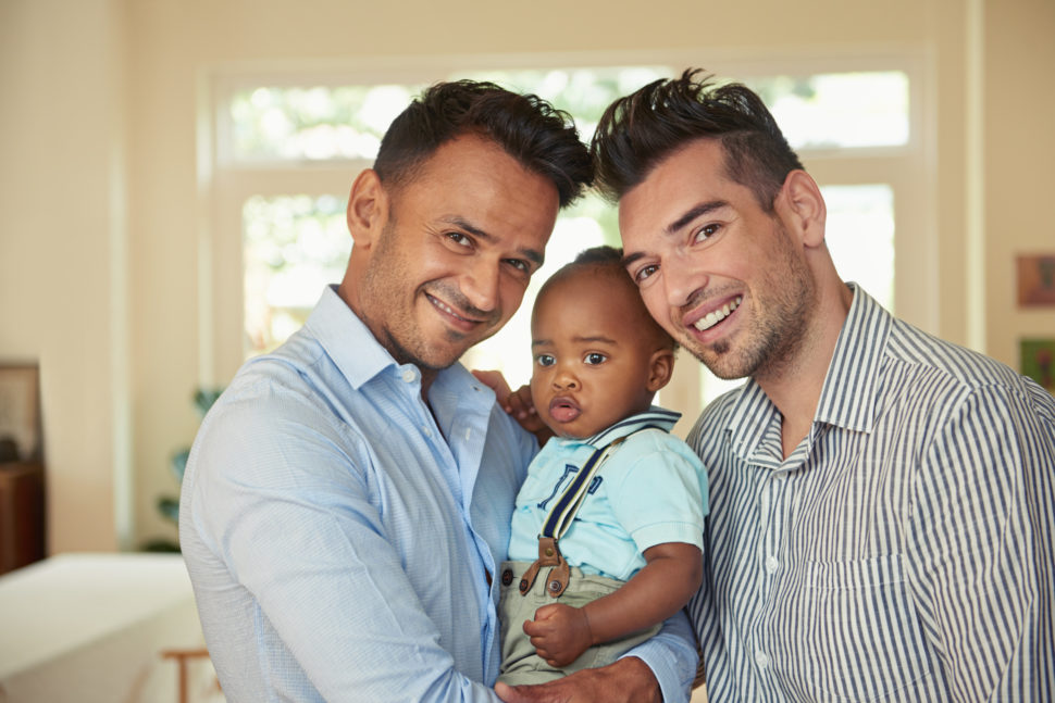 LGBT family - Two gay men cradling an adopted child
