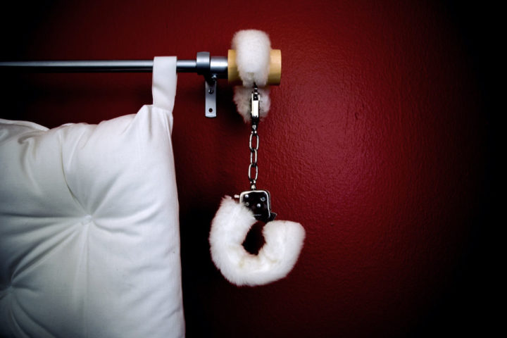Fluffy white handcuffs for kink hanging at a bedside