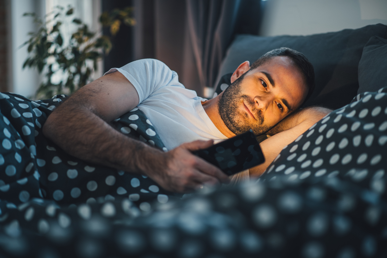 Attractive man in bed scrolling through hookup apps